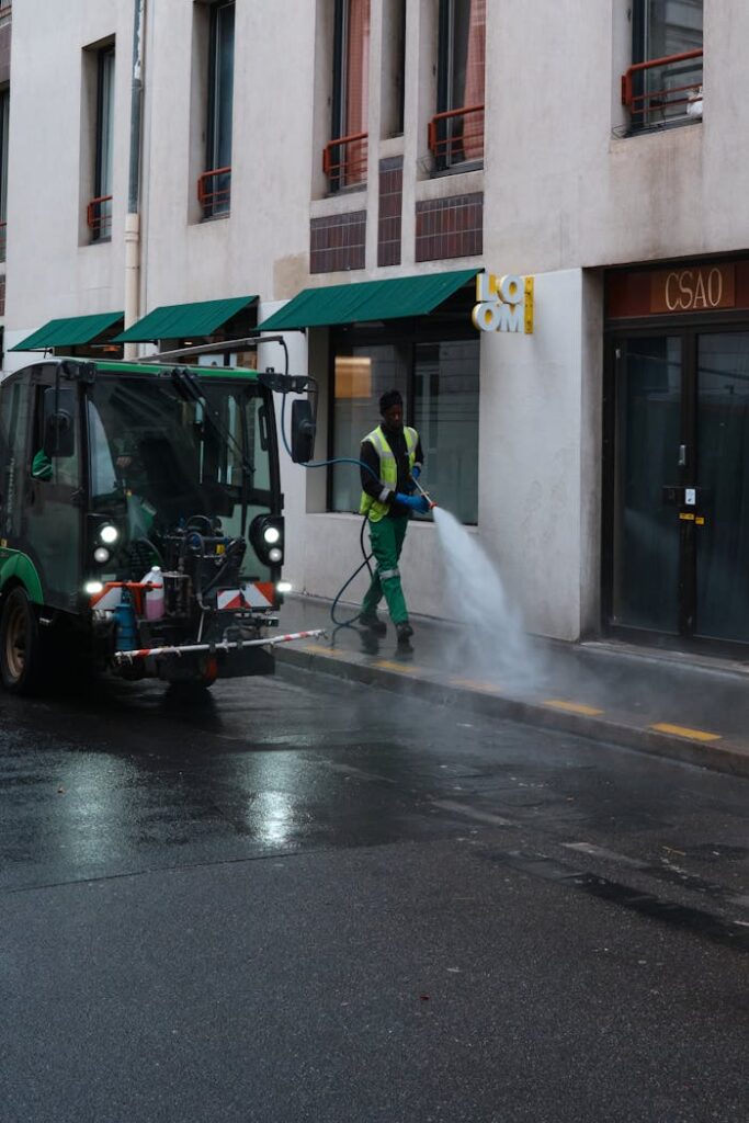A street cleaner operates a water spray machine on a city sidewalk, showcasing urban maintenance.