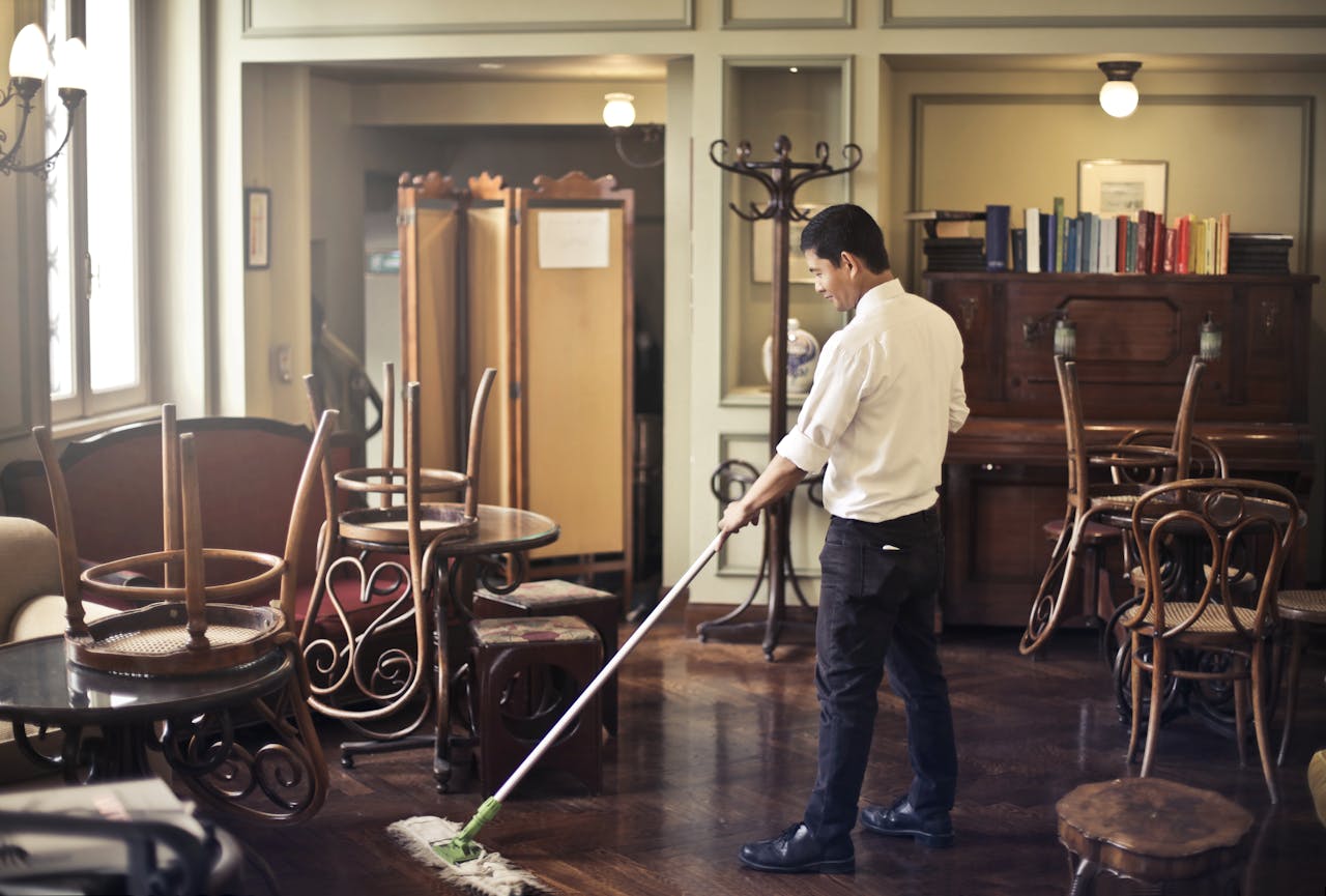 Side view of young ethnic male in uniform cleaning floor with mop while working in retro styled restaurant